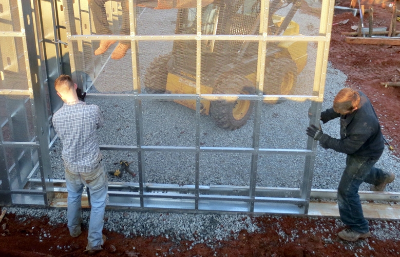 Placement of a below-grade wall panel in footer panel tray on gravel based, in preparation for slab pour & earth-berming